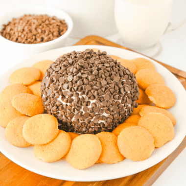 Chocolate chip cheese ball coated in mini chocolate chips on a white platter with graham crackers and pretzels