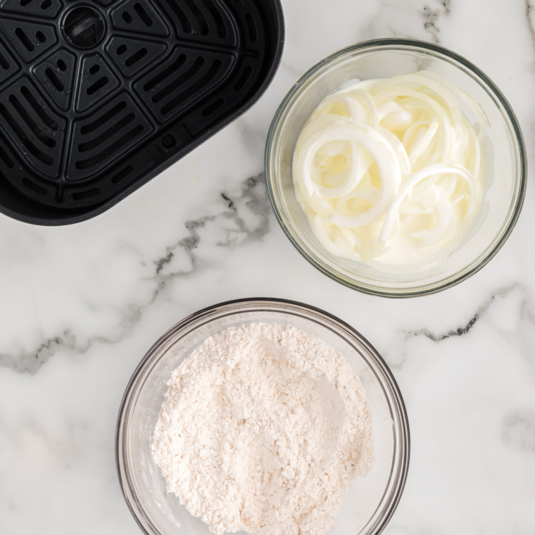 sliced onions soaking in buttermilk in a glass bowl