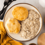 Homemade sausage gravy ladled over split biscuits with visible black pepper
