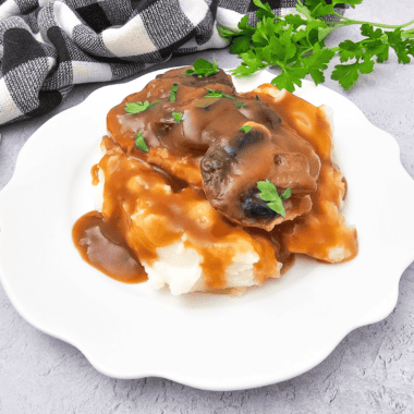 Copycat McCormick turkey gravy poured over a plate of creamy mashed potatoes