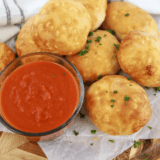 Copycat Pizza Hut pizza sauce in a small bowl with pizza rolls on a wooden table