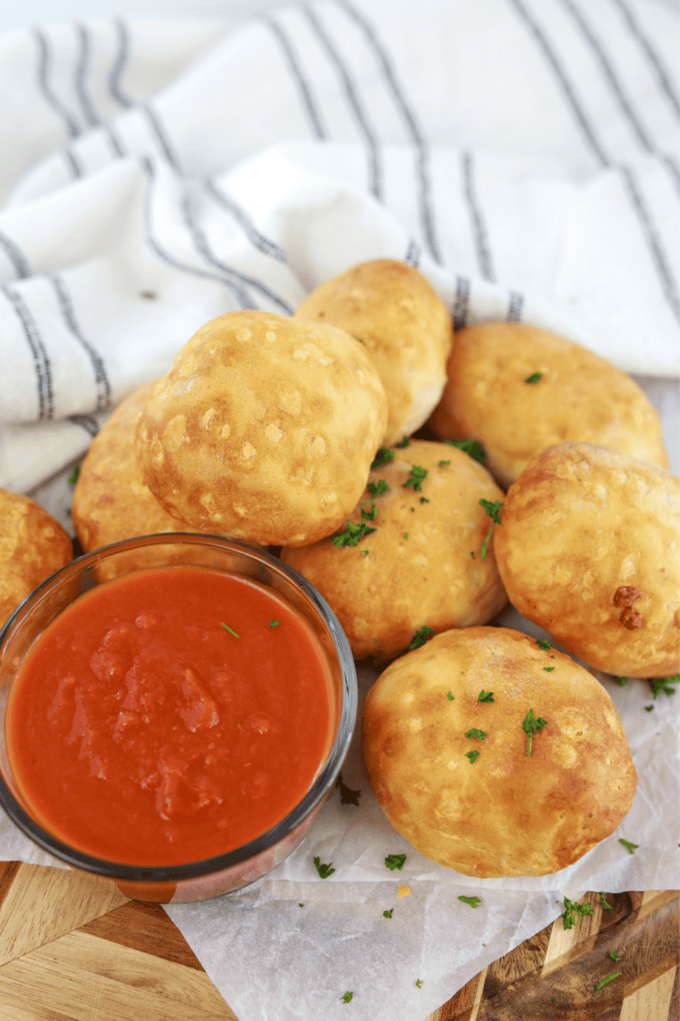 Bowl of copycat Pizza Hut pizza sauce surrounded by golden pizza rolls on a rustic table