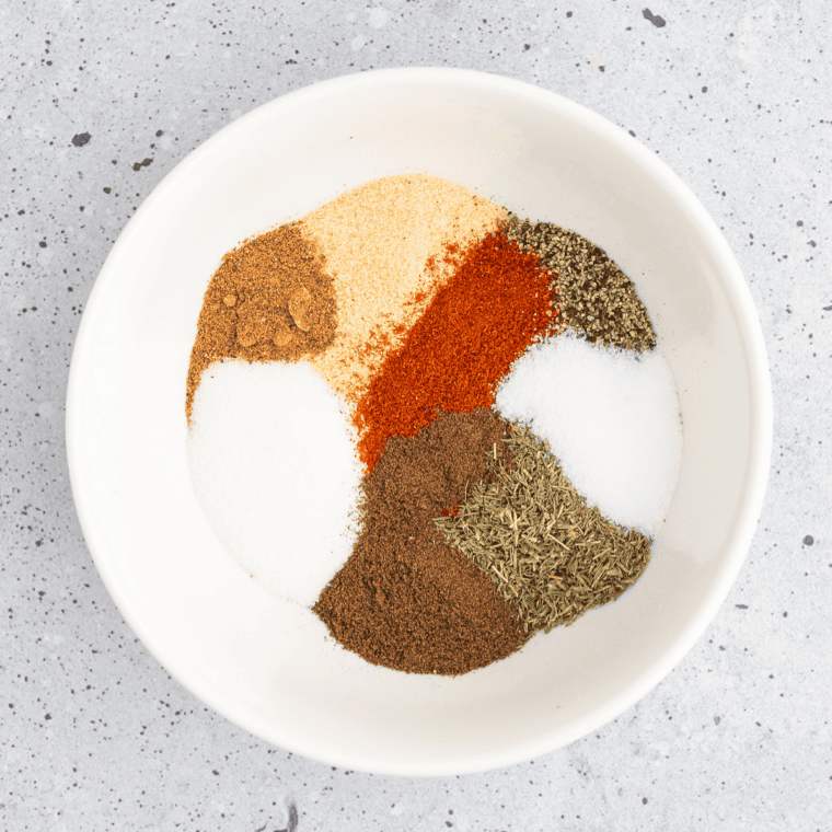 Bowl of copycat Ruth's Chris steak seasoning beside a raw ribeye coated in the spice blend