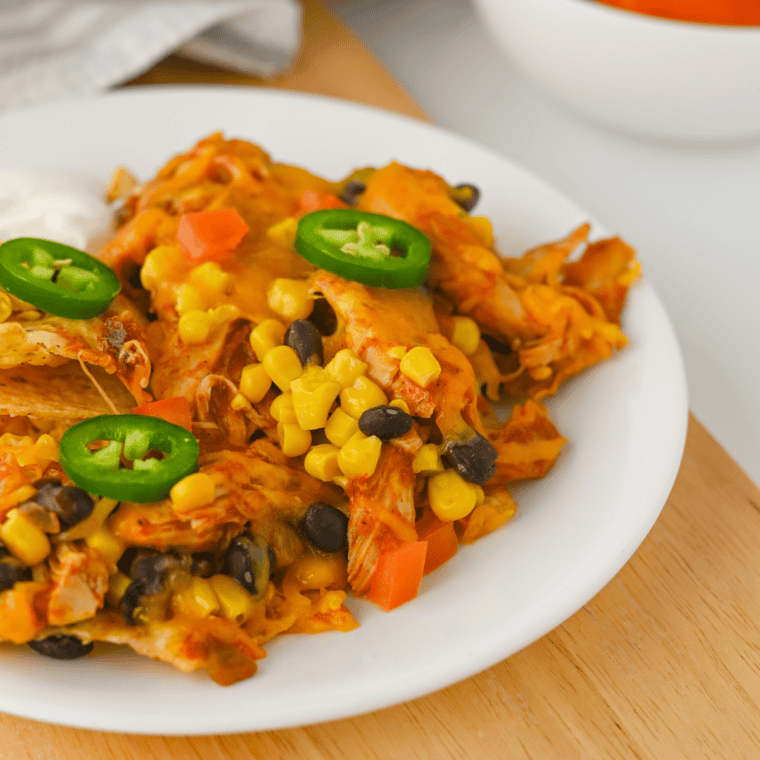 Overhead view of crockpot chicken nachos topped with shredded chicken, cheese, corn, black beans, tomatoes, and jalapeños