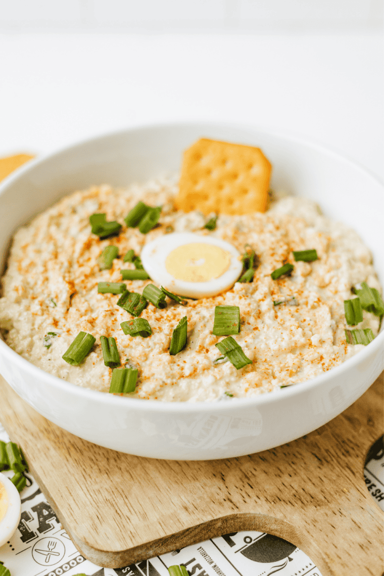 Creamy no-peel deviled egg dip garnished with smoked paprika, surrounded by assorted crackers on a wooden board