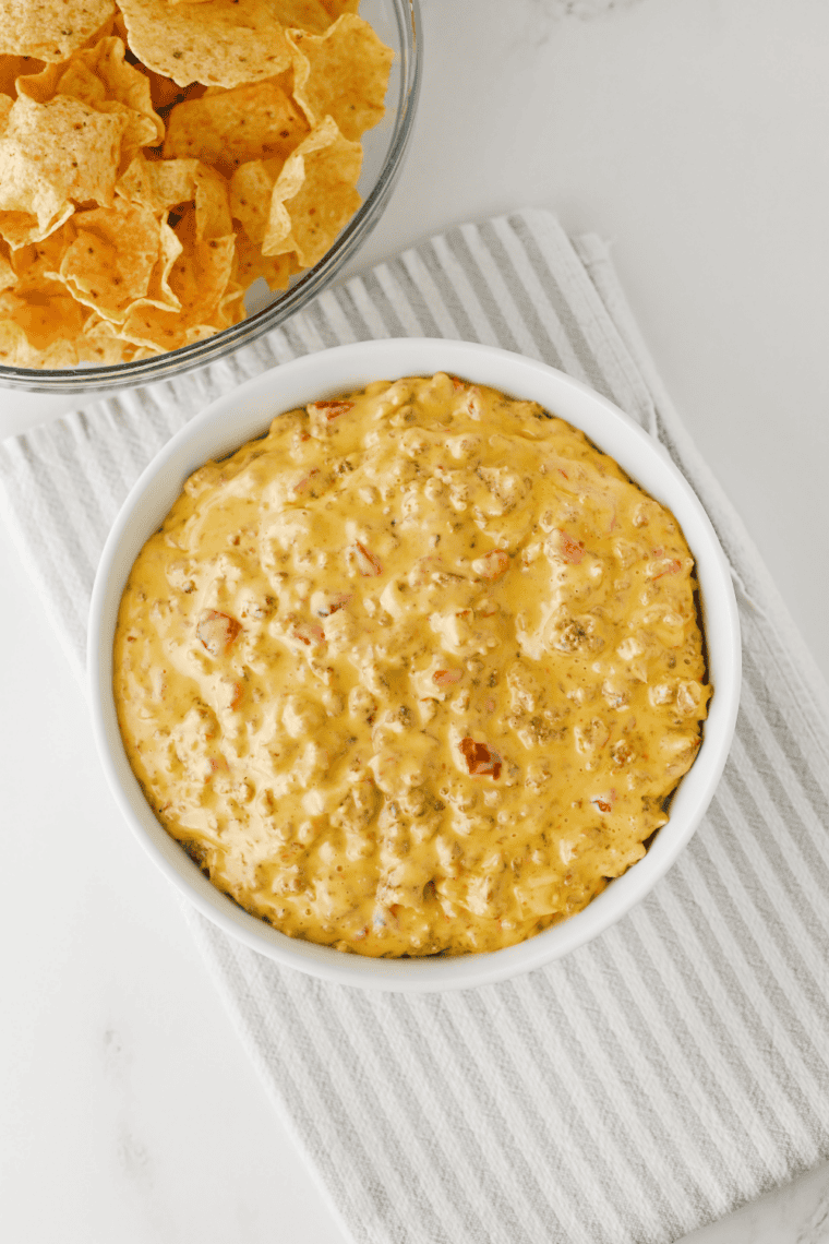 Corn chip scooping creamy football dip with visible sausage crumbles and Rotel tomatoes