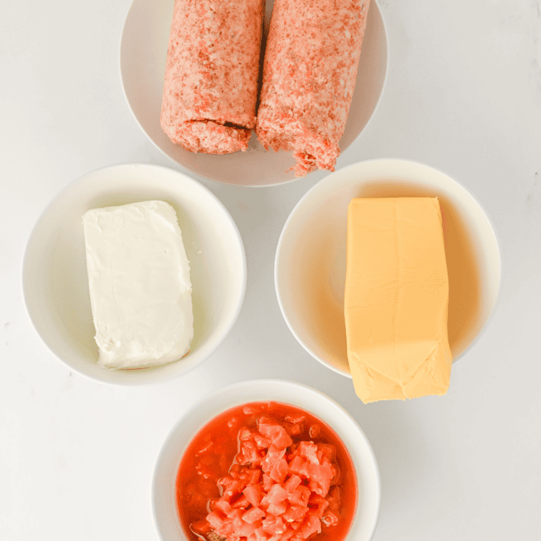 Football dip ingredients: pork sausage, a block of Velveeta, cream cheese and a can of Rotel on a marble counter