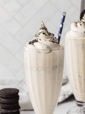 Ninja Creami Copycat Sonic Oreo Cheesecake Milkshake in a tall glass topped with whipped cream, crushed Oreos, and graham cracker crumbs
