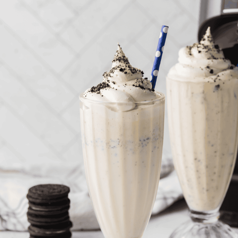 Ninja Creami Copycat Sonic Oreo Cheesecake Milkshake in a tall glass topped with whipped cream, crushed Oreos, and graham cracker crumbs