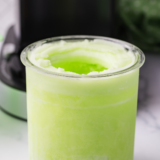 Two scoops of bright green Ninja Creami lime Italian ice in a chilled glass bowl, garnished with a fresh lime wheel