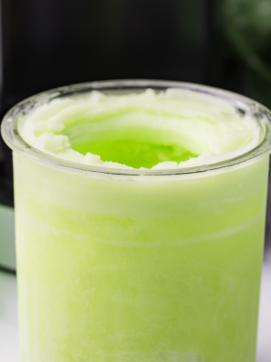 Two scoops of bright green Ninja Creami lime Italian ice in a chilled glass bowl, garnished with a fresh lime wheel