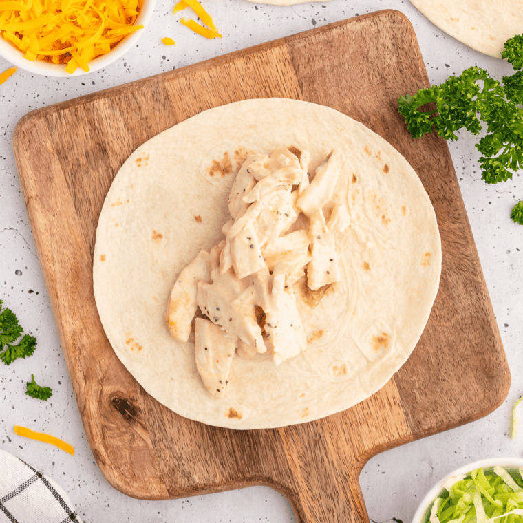 Stack of flour tortillas on a plate covered with a damp paper towel before microwaving