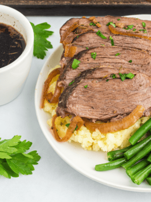 Sliced slow cooker tri tip on a wooden board with brown gravy and fresh rosemary