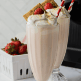 Two glasses of homemade Ninja Slushi strawberry milkshake with striped straws and fresh berries