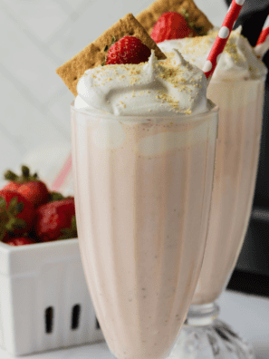 Two glasses of homemade Ninja Slushi strawberry milkshake with striped straws and fresh berries